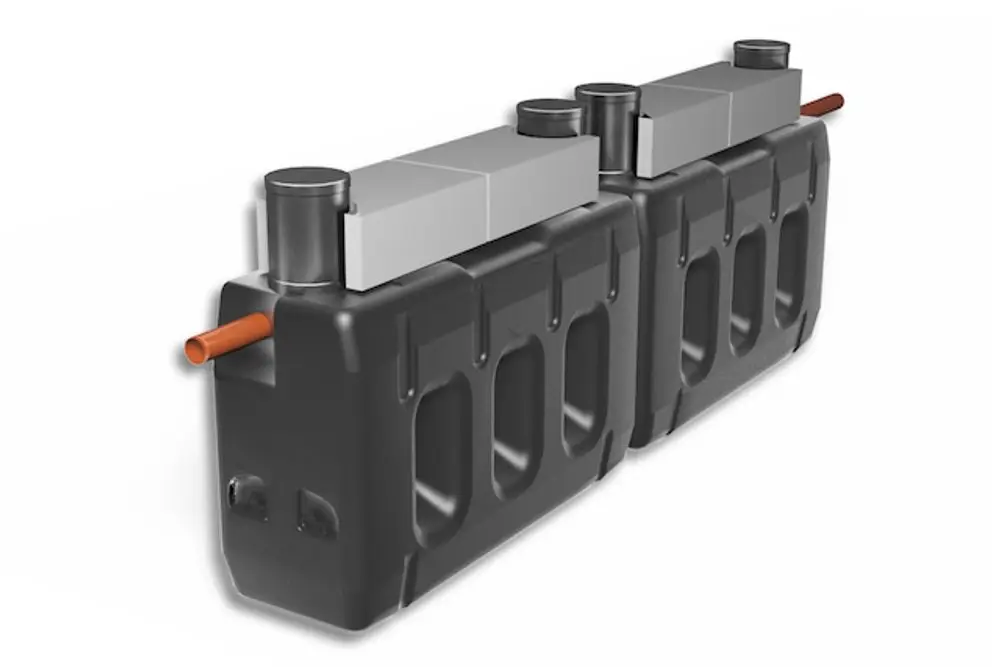 Roth Klärbehälter mit zwei schwarzen Behältern, verbunden durch ein Metallteil, mit Rohren für Ein- und Auslass. Die Konstruktion ist funktional und robust gestaltet.